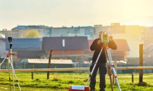 Land surveyor using tripod equipment to conduct a boundary line survey near urban redevelopment area