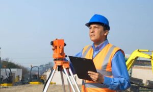 Licensed land surveyor conducting a construction survey with tripod equipment on a large development site