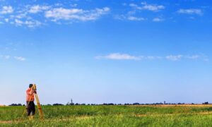 Land surveyor using GPS equipment in an open field under a bright blue sky