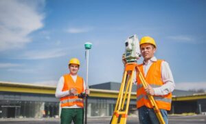 Two land surveyors conducting a site survey in front of a commercial property in Ohio using modern equipment
