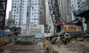 Construction workers and heavy machinery at an urban building site conducting ALTA Land Title Surveys amid tall residential buildings, highlighting infrastructure development.