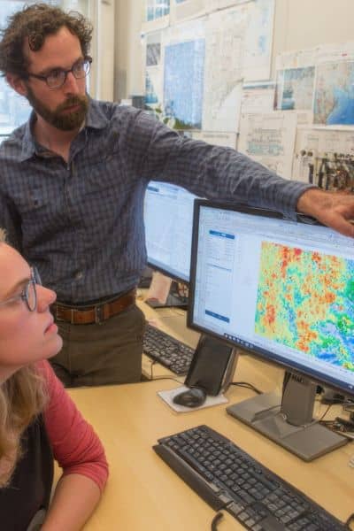 A team of land surveying professionals reviewing GNSS mapping data on a computer to improve workflow efficiency