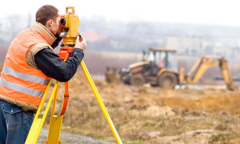 A construction surveyor using a total station to check site layout before excavation begins