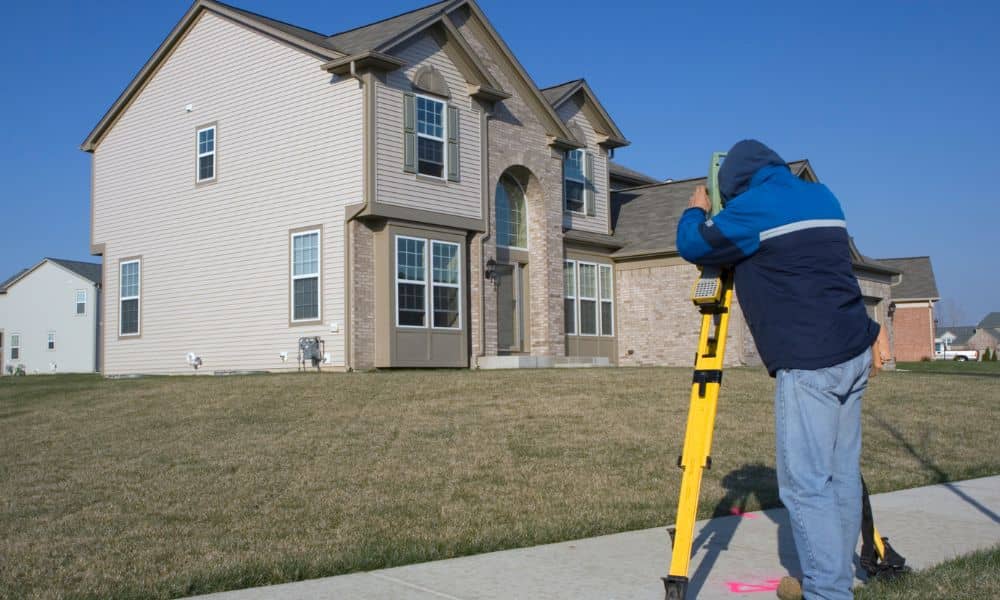 A local surveyor measuring a residential property line near a suburban home