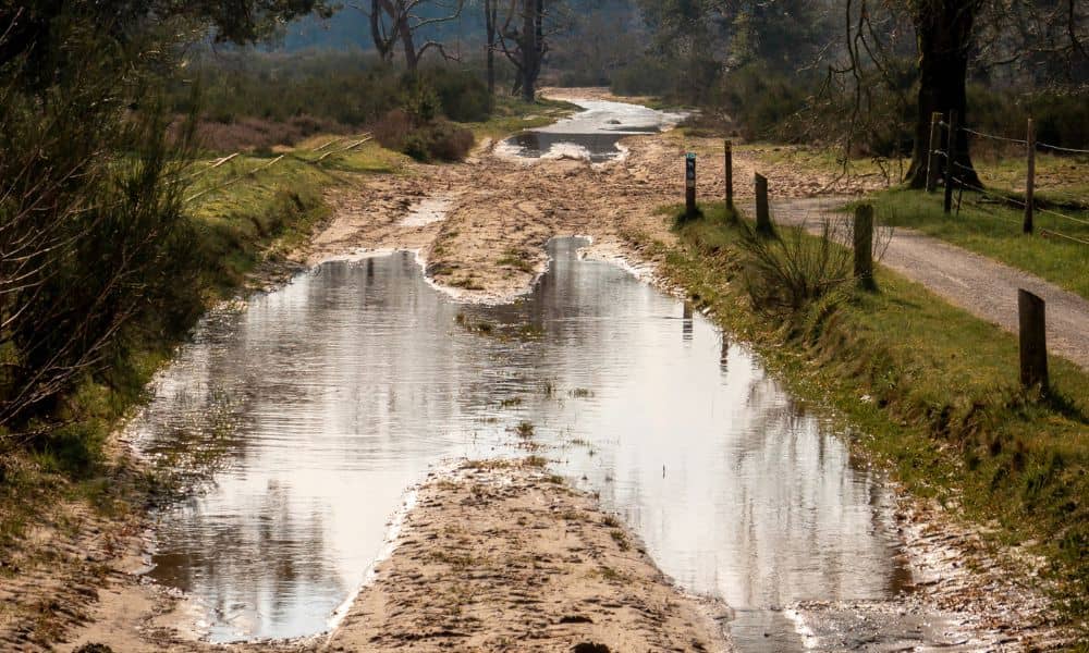 Muddy road with standing water after flooding showing ground changes and need for a topographic survey