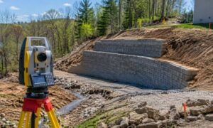 Topographic survey equipment measuring a sloped site before retaining wall construction for accurate grading and drainage planning