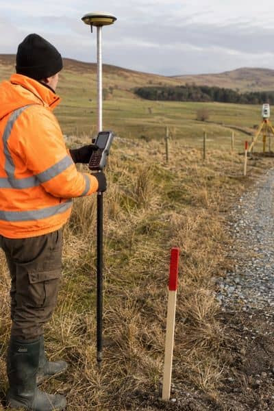 Land surveyor using GPS equipment to verify property boundaries and access conditions on a rural parcel